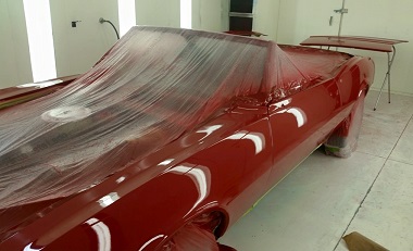 paint booth with red classic car in process of being painted; there is a protective covering over parts that should not be painted